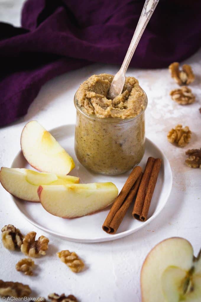 Jar of walnut butter with apples, walnuts, and cinnamon sticks surrounding it