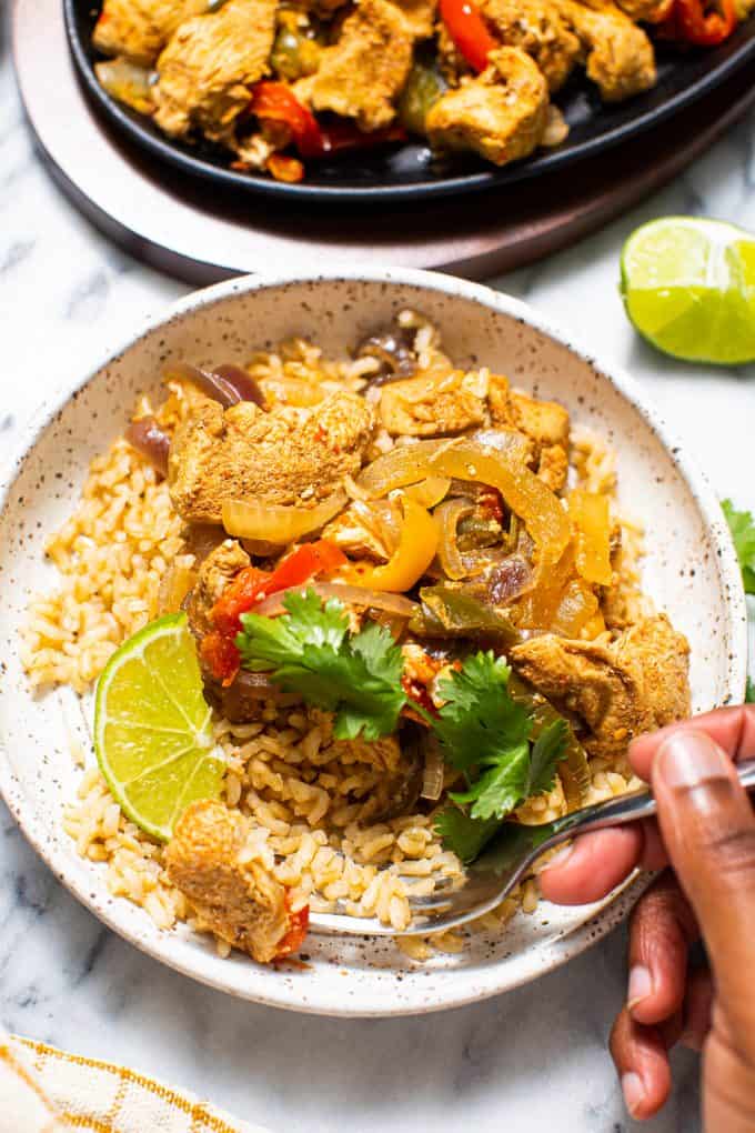 Bowl of slow cooker/crockpot chicken fajitas over rice with a hand holding a fork