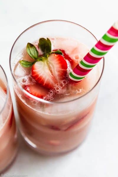Homemade pink drink recipe in a glass with strawberry slices and a straw