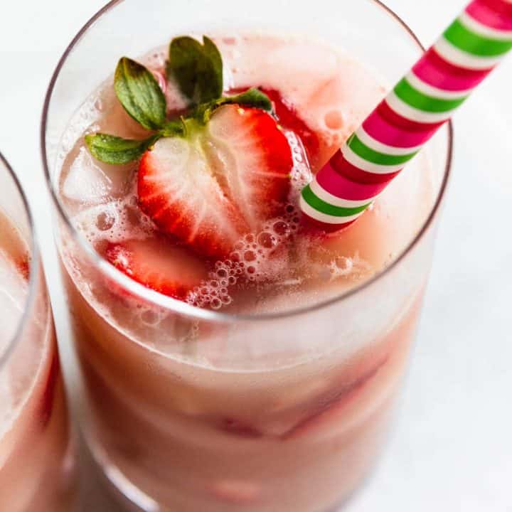 Homemade pink drink recipe in a glass with strawberry slices and a straw