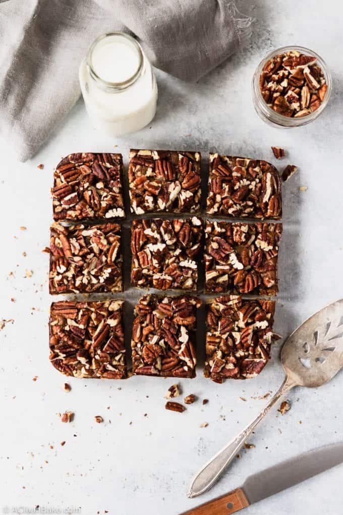 Batch of sliced gluten free and paleo pecan bars on a table with milk and a serving spatula