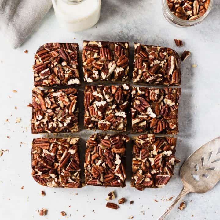 Batch of sliced gluten free and paleo pecan bars on a table with milk and a serving spatula