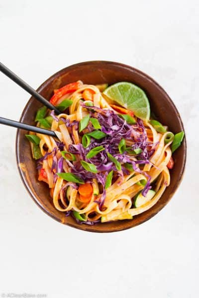 gluten free curry noodles in a bowl topped with a lime wedge, shredded red cabbage, and sliced scallions