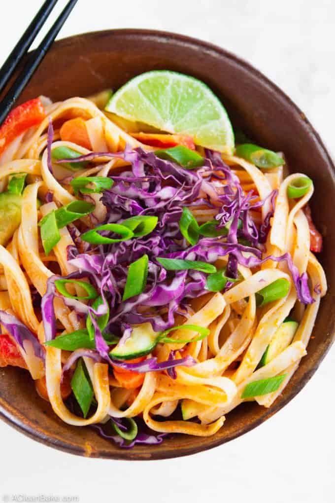gluten free curry noodles in a bowl topped with a lime wedge, shredded red cabbage, and sliced scallions