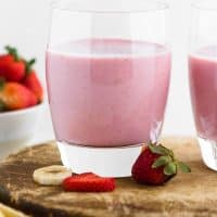 Strawberry Banana Smoothie with Added Protein in a cup sitting on a cutting board surrounded by fruit