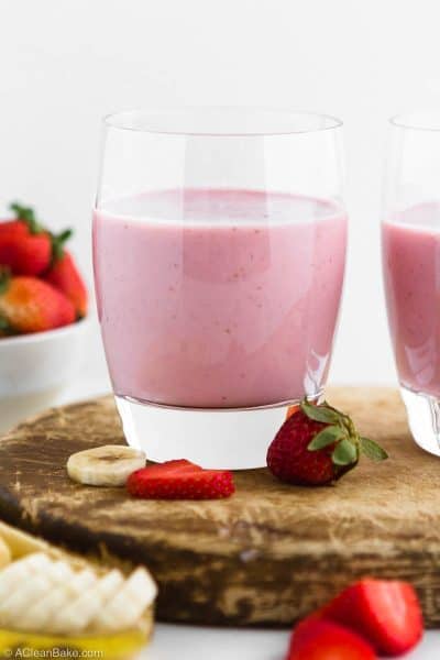 Strawberry Banana Smoothie with Added Protein in a cup sitting on a cutting board surrounded by fruit