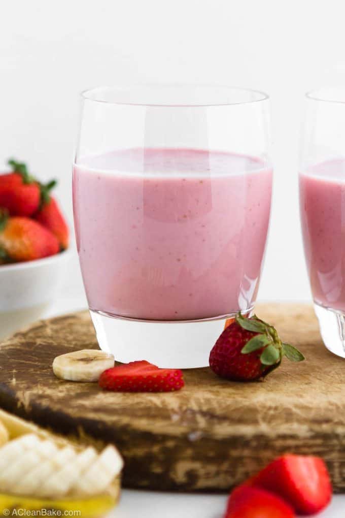 Strawberry Banana Smoothie med tilsat protein i en kop, der står på et skærebræt omgivet af frugt