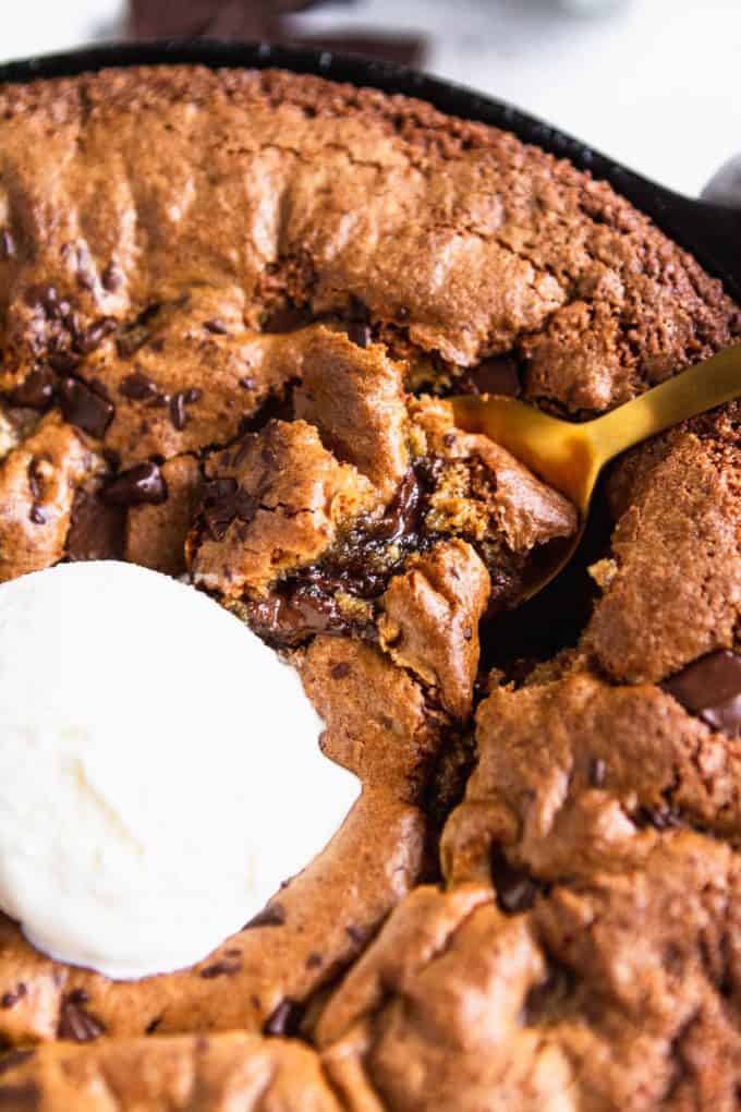 Deep dish chocolate chip skillet cookie (gluten free and paleo) in a skillet with a scoop of ice cream and a spoon