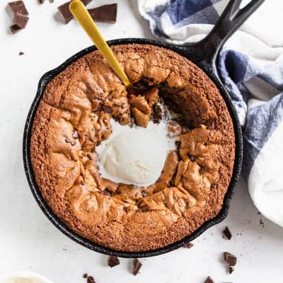 Deep dish chocolate chip skillet cookie (gluten free and paleo) in a skillet with a scoop of ice cream and a spoon