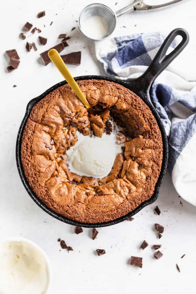 Deep dish chocolate chip skillet cookie (gluten free and paleo) in a skillet with a scoop of ice cream and a spoon