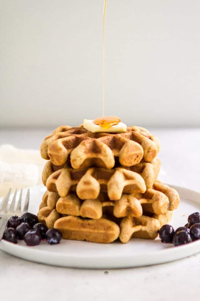 Stack of paleo gluten free waffles on a plate with a drizzle of syrup hitting the top