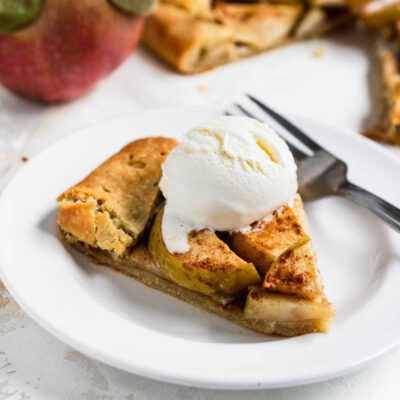 Slice of paleo gluten free apple galette on a plate topped with ice cream and apples in the background