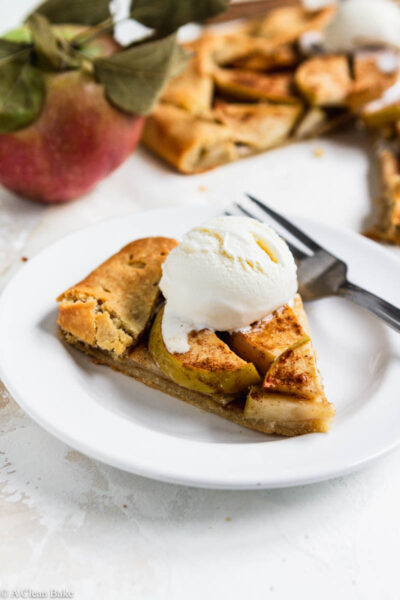 Slice of paleo gluten free apple galette on a plate topped with ice cream and apples in the background