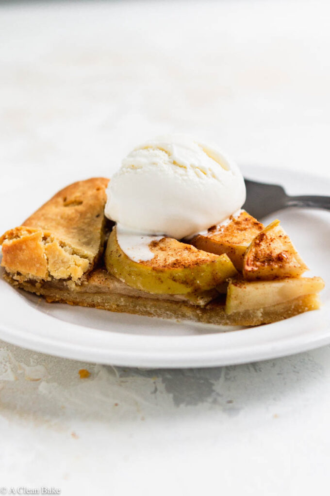 Slice of paleo gluten free apple galette on a plate topped with ice cream on a white backgound