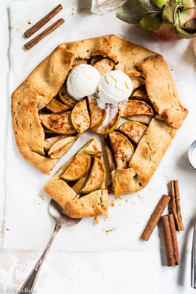 Paleo gluten free apple galette on a white table with ice cream and a slice being removed with a spatula
