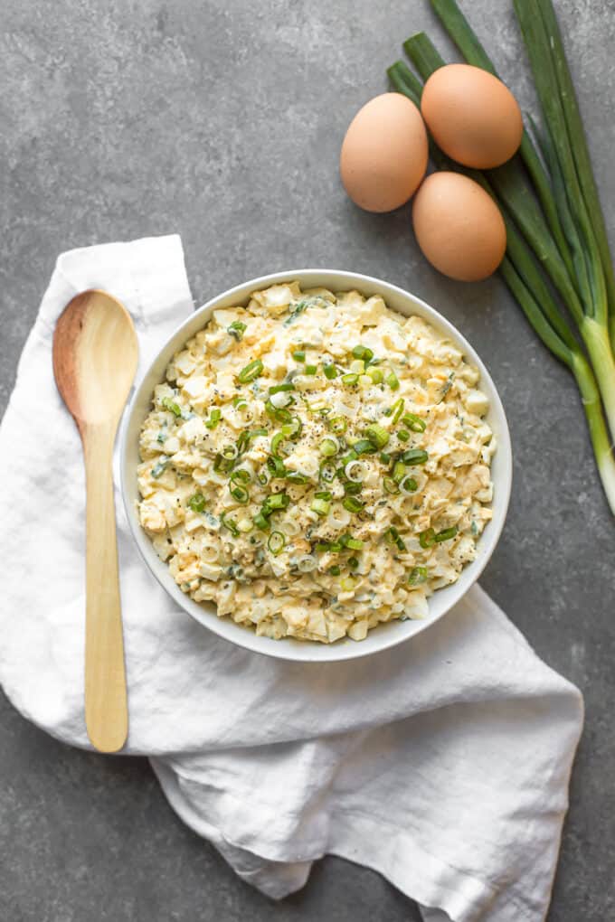 Egg salad on a table with eggs and scallions around it