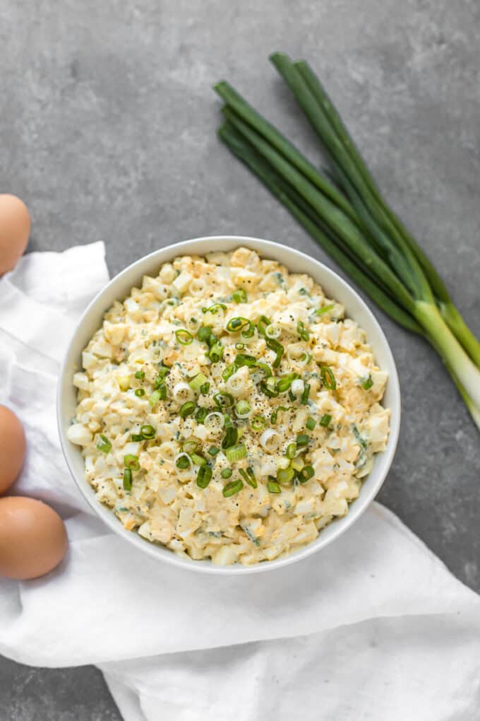 Egg salad on a table with eggs and scallions surrounding it