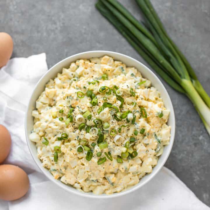 Egg salad on a table with eggs and scallions surrounding it