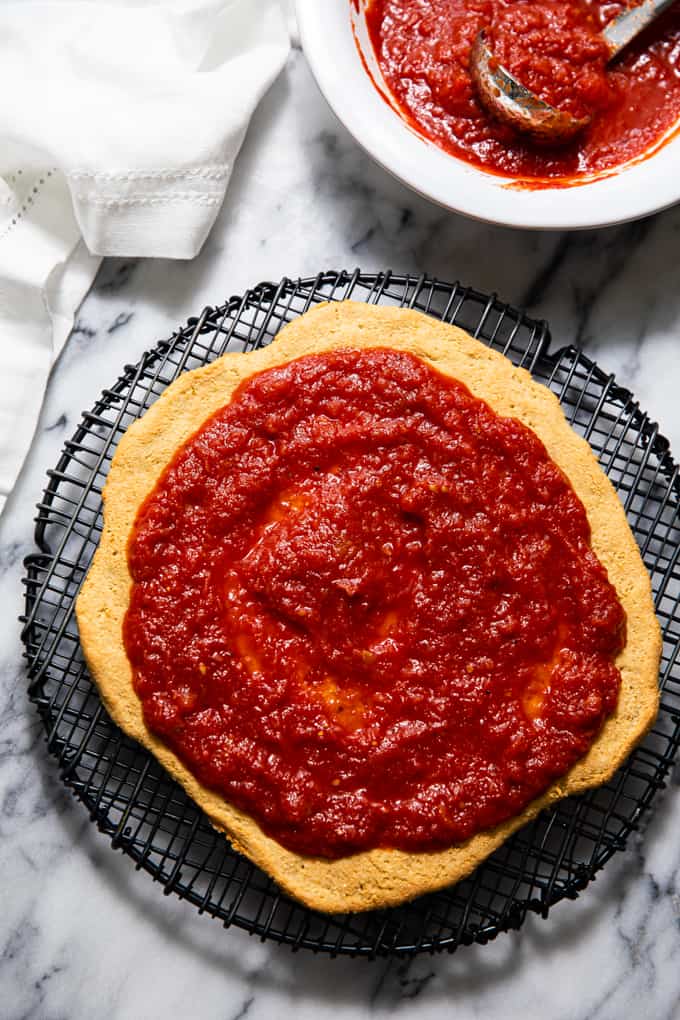 Pizza crust topped with sauce resting on a cooling rack