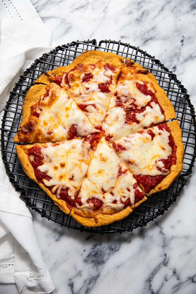 Gluten free paleo pizza crust topped with sauce and cheese on a cooling rack