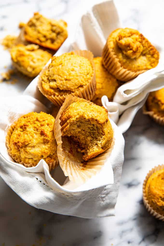 Pile of gluten free corn muffins on a marble tabletop with a bite taken out of one