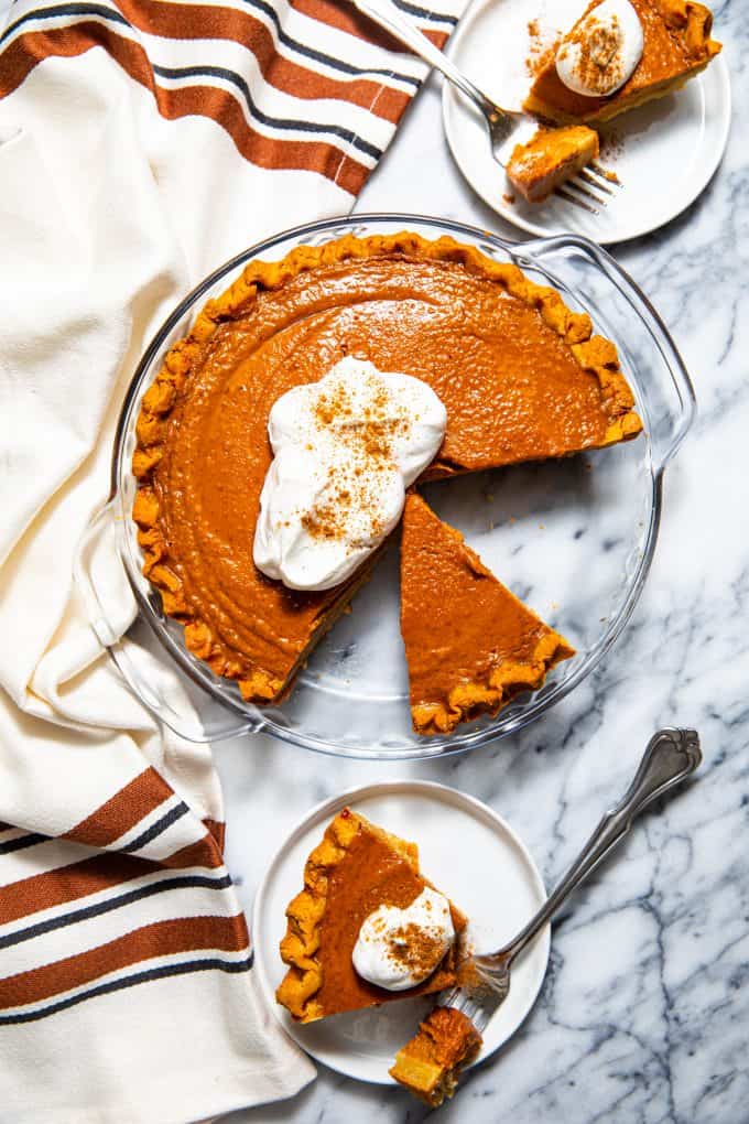 Paleo gluten free pumpkin pie from above topped with whipped cream, and a slice next to it on a plate
