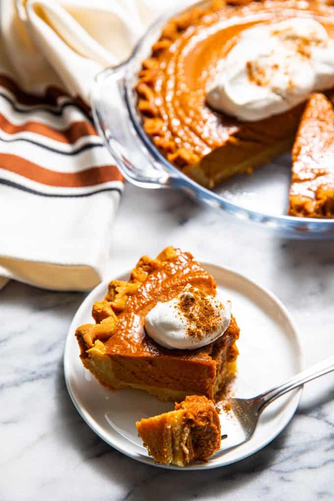 Slice of paleo gluten free pumpkin pie on a plate with a fork in front of a pie plate