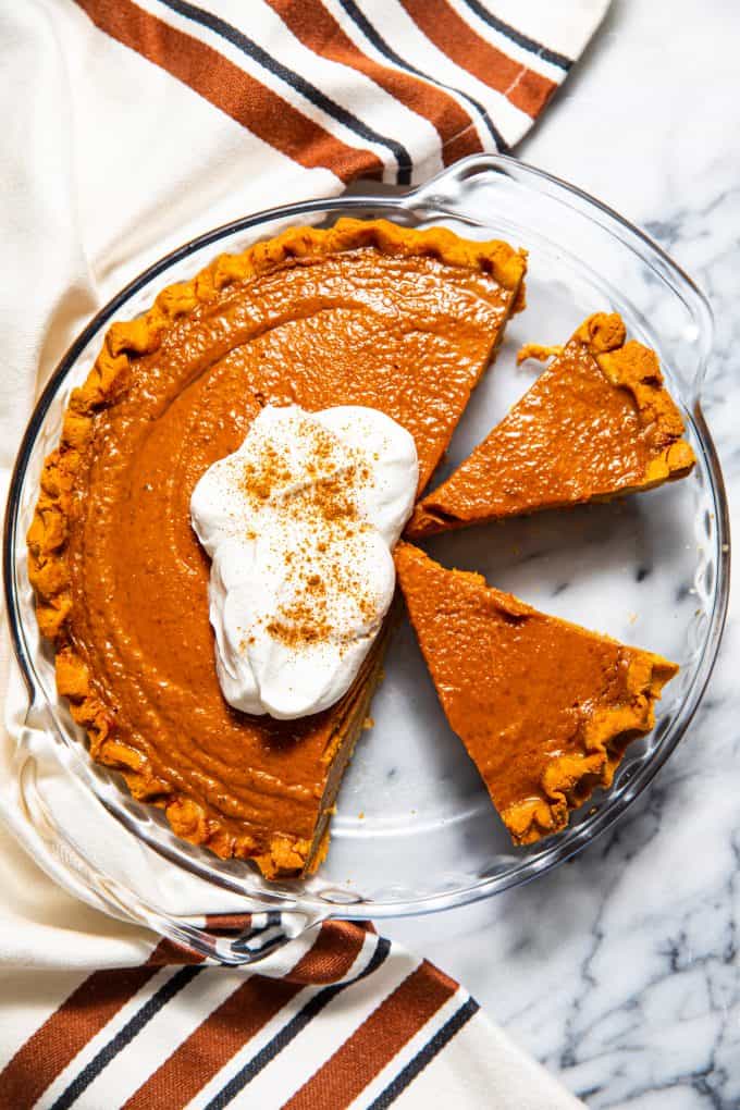 Paleo gluten free pumpkin pie from above topped with whipped cream, and a few slices cut out